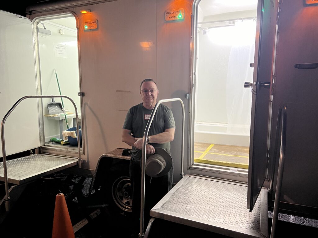 A man from Severna Park United Methodist Church standing in front of a shower trailer. The shower trailer is used to provide showers to people who are homeless
