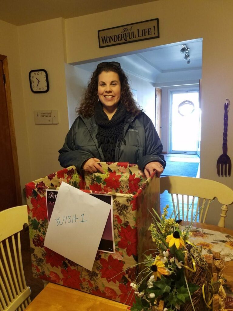 A white women who is a volunteer standing over a box decorated with Christmas wrapping paper. 