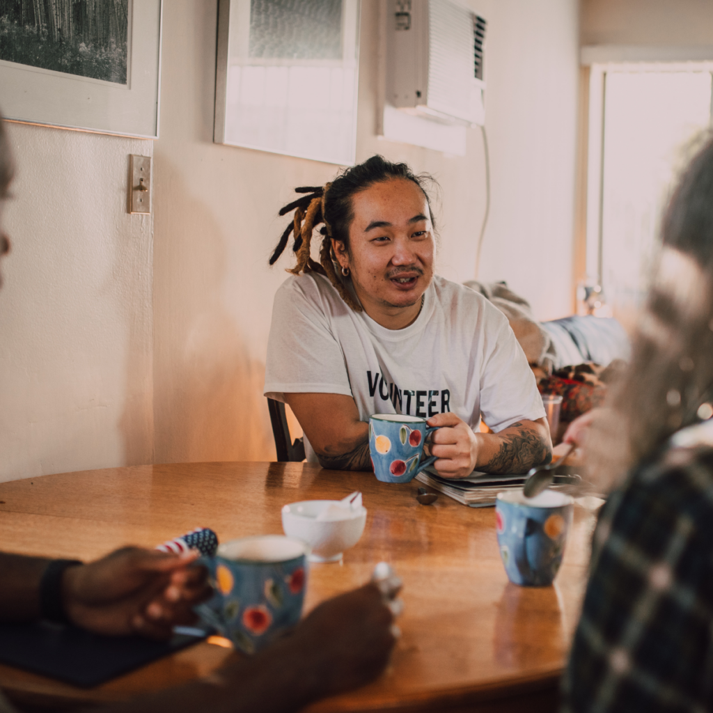 A volunteer sitting at a table talking a man who recently moved into an apartment after being homeless. Social connection with other and with the community is important to people leaving homelessness. 