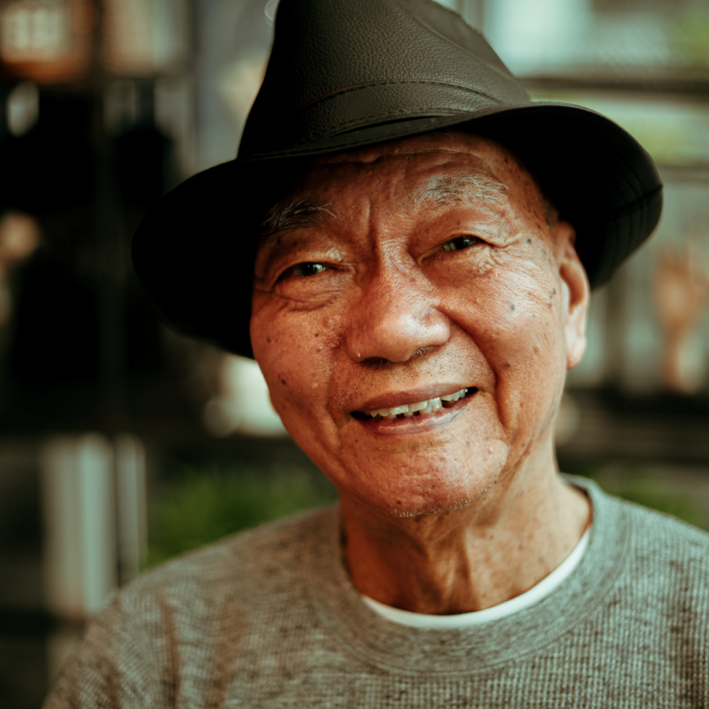 An older Asian man smiling. He is wearing a hat. People of all races and ethnicities can become homeless. 