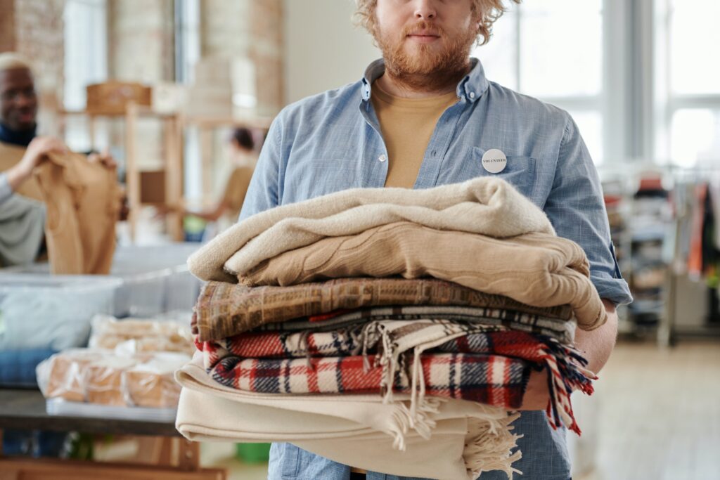 A white man with red hair holds folded blankets. Winter Relief emergency shelter always needs blankets.