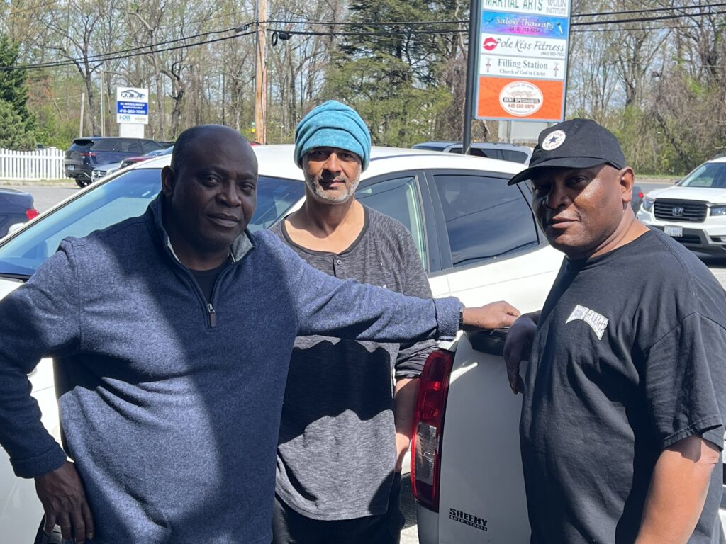 Three men, Kevin, T.J, and Naveen, standing around a white truck. The men are staff members who helped move the Arundel House of Hope offices. 